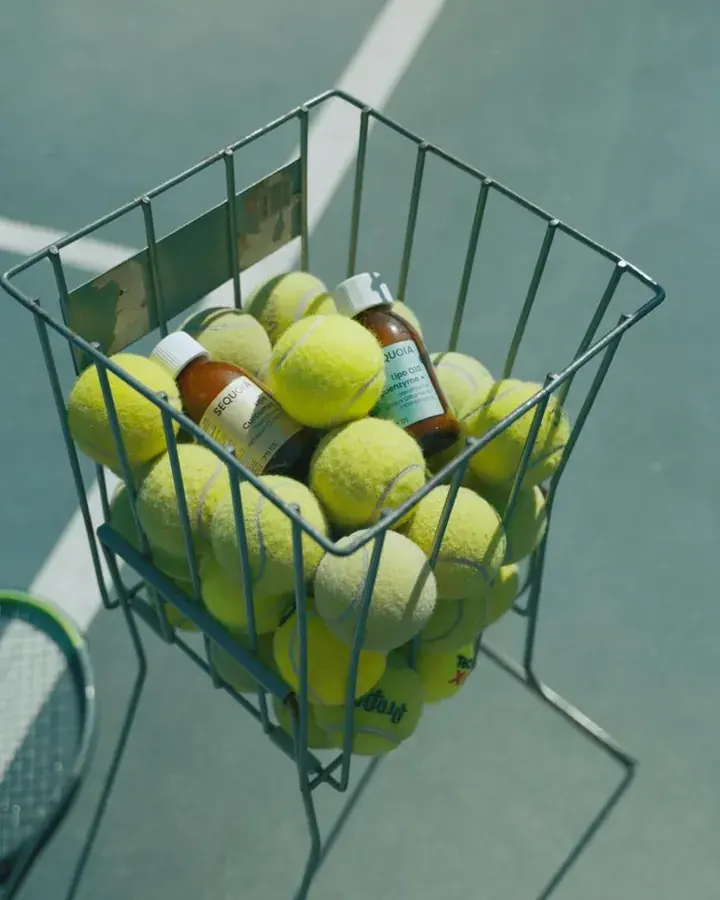 Small bottles among tennis balls in a wire basket on a court